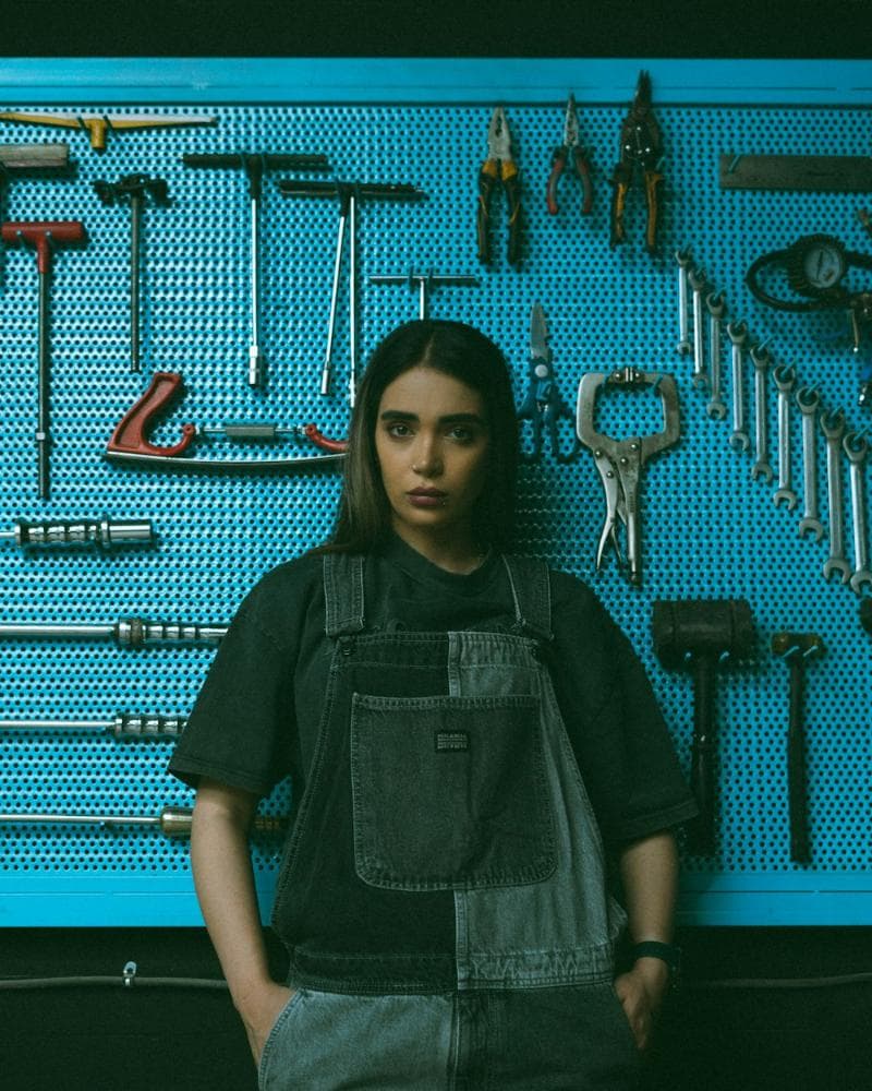 Crew member in overalls in front of a tool wall